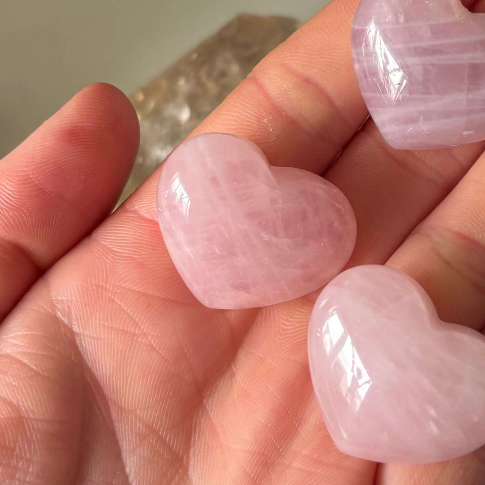 A collection of small pink rose quartz heart carvings resting in a hand, showing natural internal fractures and variations.