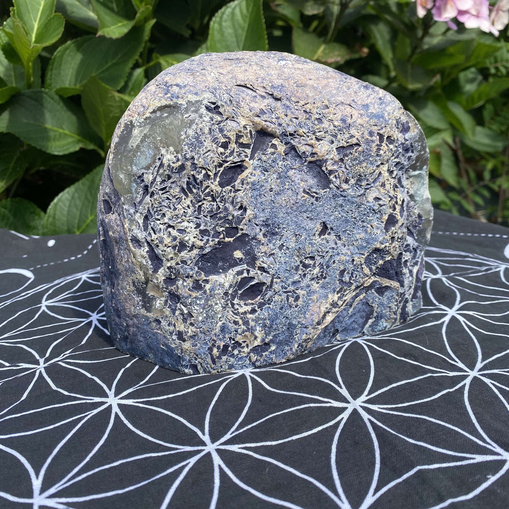 A rear view of the substantial agate specimen sitting on a black printed cloth, showcasing its unpolished rough outer geode crust. The dark charcoal back contrasts beautifully against the geometric lines, helping buyers see the stone's organic origins.
