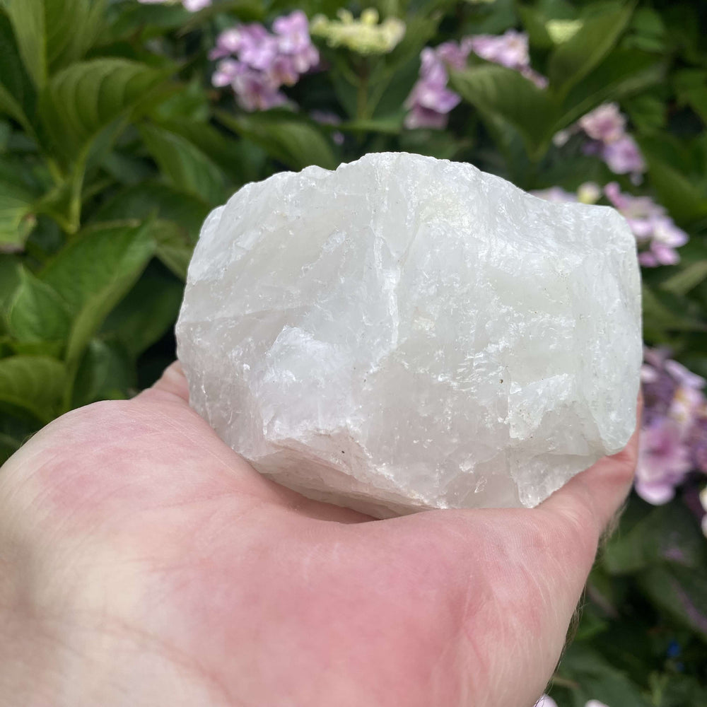A substantial rough White Quartz specimen cradled sideways in a hand outdoors. The large unpolished stone displays its intense milky white colouring, dense internal crystalline structures, and solid chunkiness under natural daylight.