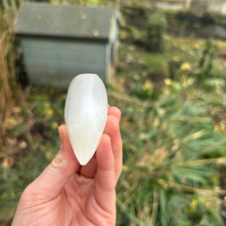 A side profile view of a polished selenite puff heart carving held in fingers, highlighting its generous 3D puffy thickness and smoothly rounded dimensional edges that feel beautifully tactile when rolled between hands.
