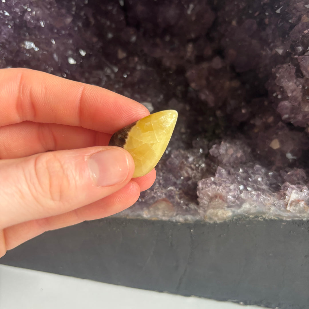 A close-up view of fingers holding the side profile edge of the septarian jasper carved tear drop stone close up, highlighting its smooth polished facets designed to bring a steady sense of physical and emotional stability.