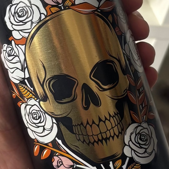 A macro view looking straight down at the metallic gold skull graphic on the black drinking flask. The sharp contrast highlights the bold lines and fine detailing of the print, serving as a mindful ritual reminder to stay grounded and align the Root and Sacral chakras.
