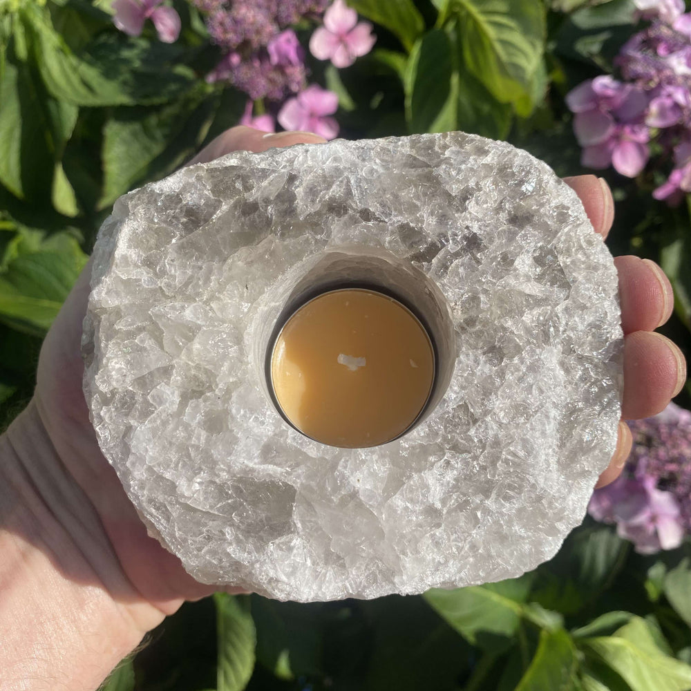 A top-down view of the rough Smokey Quartz crystal candle holder held in an open hand outdoors, highlighting the central circular slot containing a small yellow tea light candle.