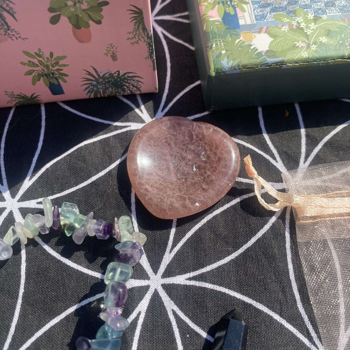 A close-up view of the smooth aventurine heart pocket stone laying beside the open illustrated gift box lid. The warm, rich earthy tones of the heart figurine reflect themes of gentle compassion, heart chakra alignment, and daily mindfulness.