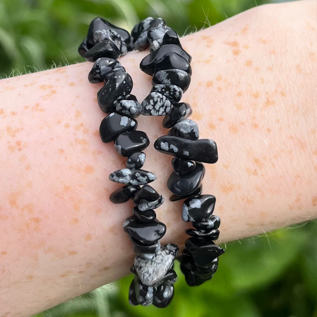 A close-up shot of a polished black Snowflake Obsidian crystal chip bracelet wrapped twice around a freckled wrist outdoors