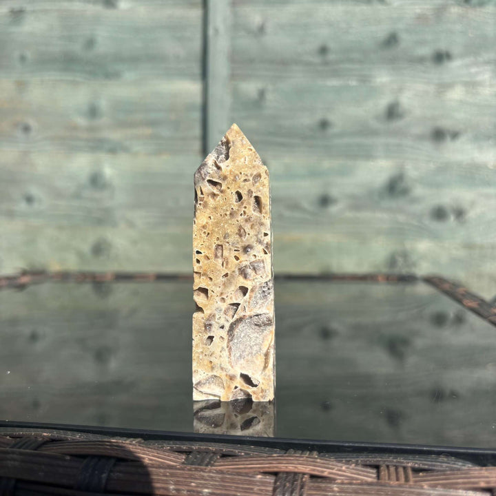 An eye-level shot showing the pointed Sphalerite crystal tower standing alone upon a reflective tabletop display. The outdoor morning sun accentuates its rich earthy patterns and unique geological birthmarks, demonstrating how it adds a steady, protective shield and a grounding presence to any creative workspace.