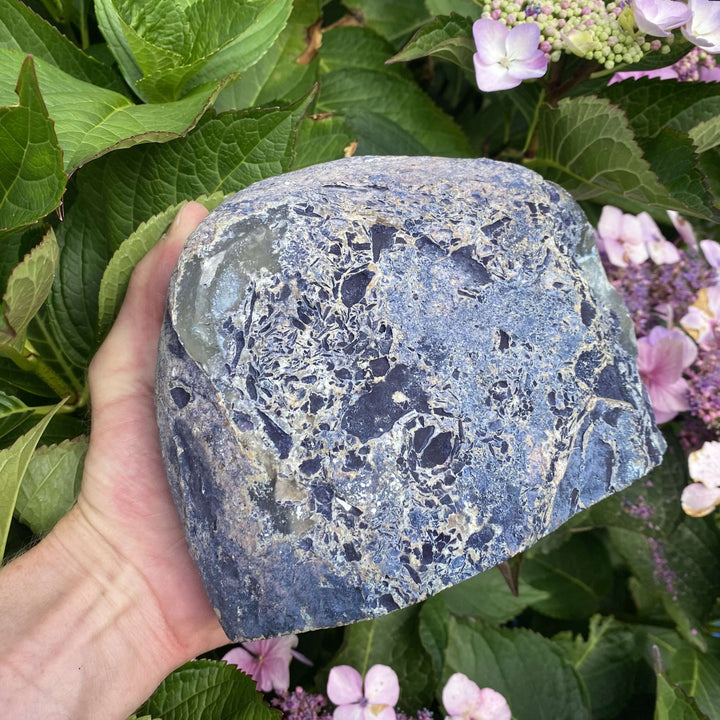 A side handheld perspective of the substantial agate display piece turned to show its thick profile width. The mixture of rugged raw matrix and glassy polished crystal facets creates an impressive mineral gift for an intentional home.