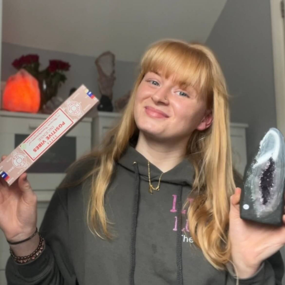 Tasha, founder of Lilz Luxe, smiling while holding a box of Satya positive vibes incense and a deep purple raw amethyst crystal geode cluster.