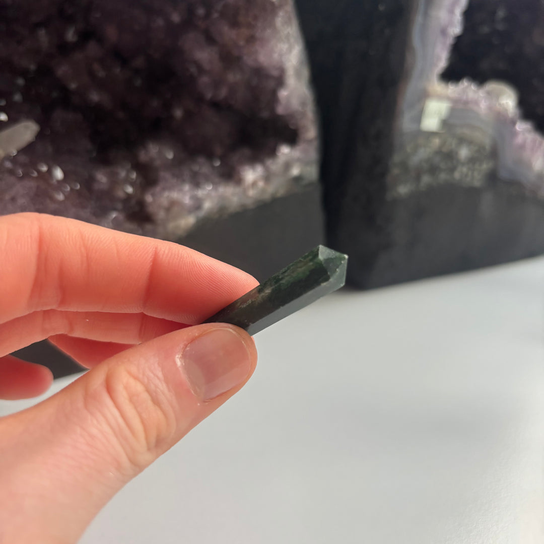 A close-up view of a hand holding the 4cm Tree Agate crystal point horizontally between fingertips to reveal its smooth contours. The double-terminated tips help move energy in both directions beautifully, inviting a lovely feeling of emotional safety and Heart Chakra balance.