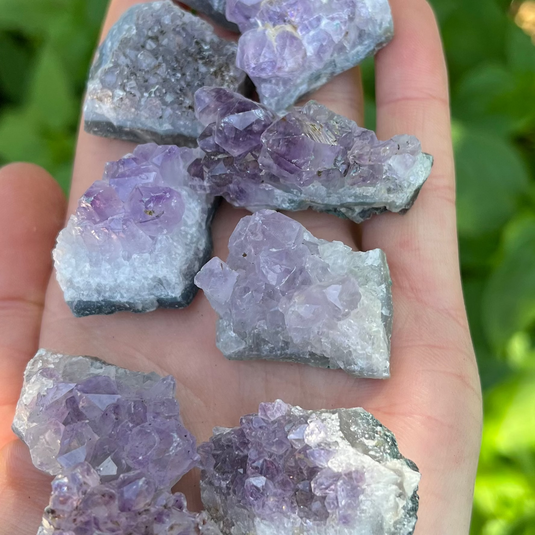 A tight macro shot focusing on the jagged edges and rich purple colour gradients of the miniature Amethyst crystal clusters in a hand. The composition beautifully displays the natural crystalline structures and rough geological foundations unique to each individual pocket stone.
