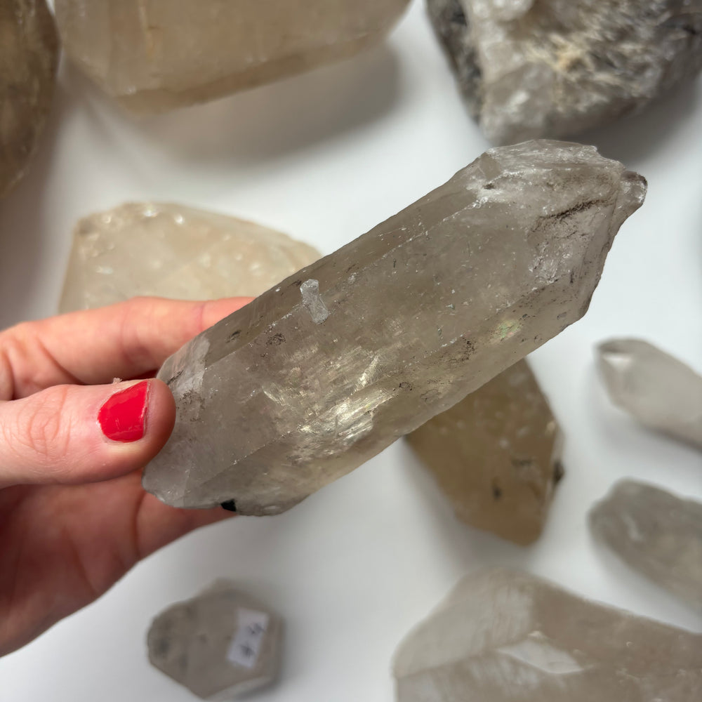 A close-up view of a hand holding an unpolished clear quartz raw point horizontally, detailing the unique geological frost variations and textured natural contours that help clear away mental static and uplift the frequency of your home space.