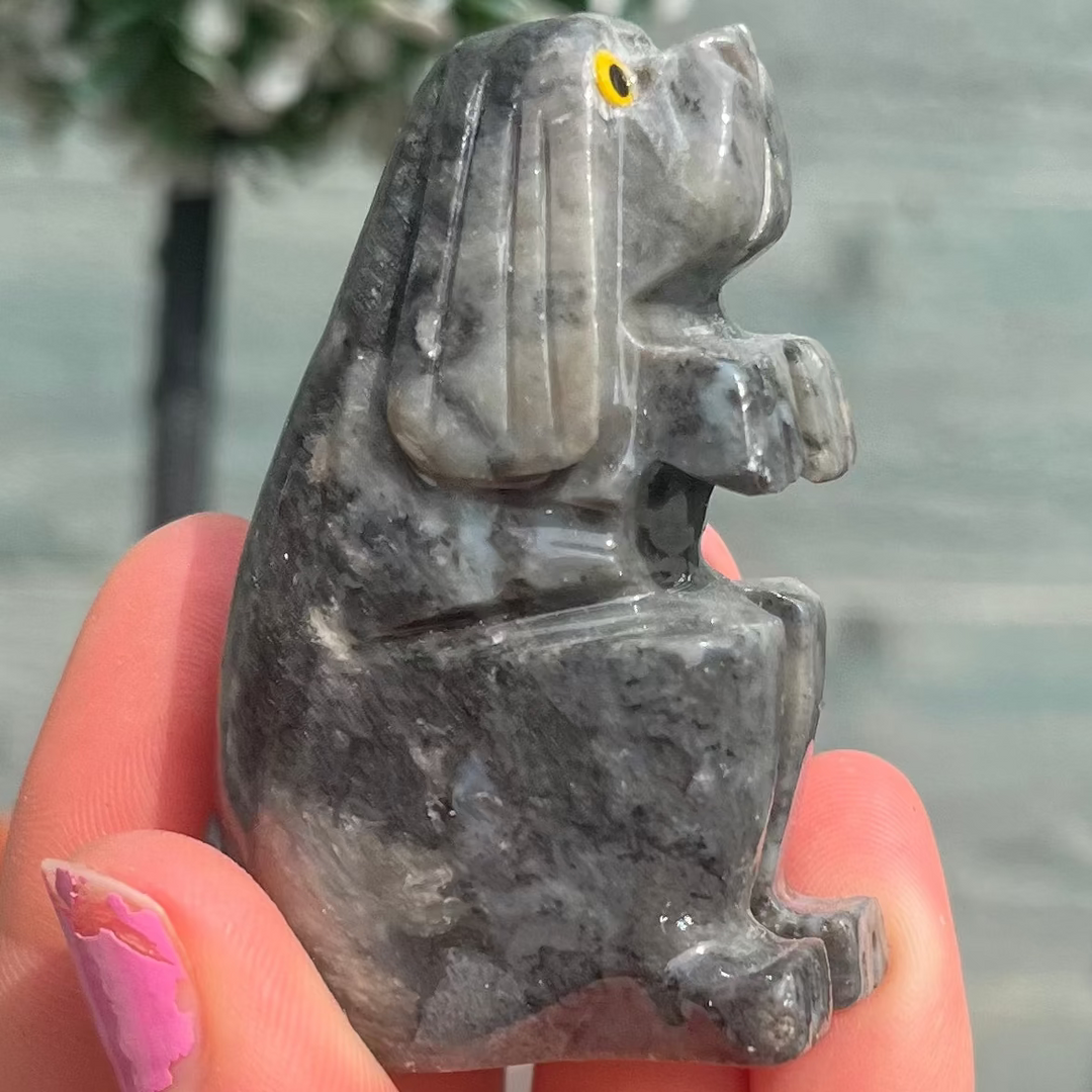 A close-up lifestyle shot of the grey soapstone canine talisman held gently in an open palm. The smooth contours and detailed long ears are beautifully captured under soft lighting, demonstrating its comforting tactile feel as an everyday pocket stone.