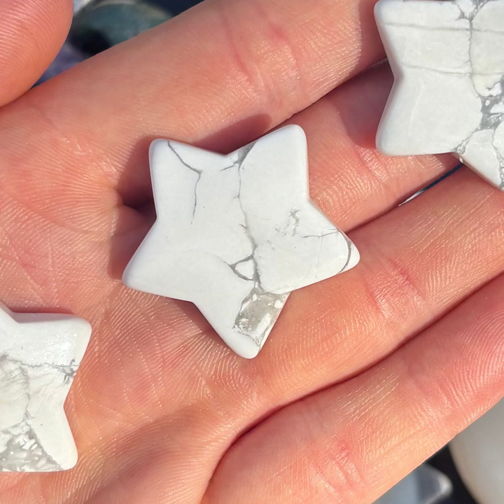 A close-up view of a single polished white howlite pocket star resting securely between fingers, highlighting the delicate webbed marbling patterns that serve as a comforting tactile anchor to quiet an overactive mind during times of stress.