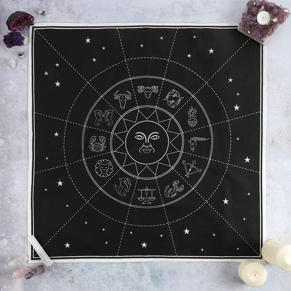 A black cotton altar cloth with a white zodiac chart design, displayed on a wall with candles and crystals.