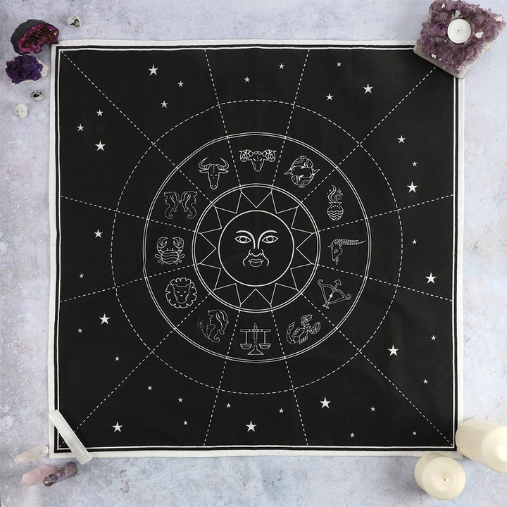 A black cotton altar cloth with a white zodiac chart design, displayed on a wall with candles and crystals.