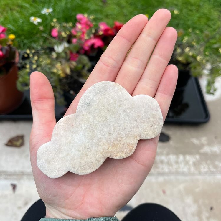 A pink amethyst crystal figure shaped like a cloud held in a hand, with green plant background.