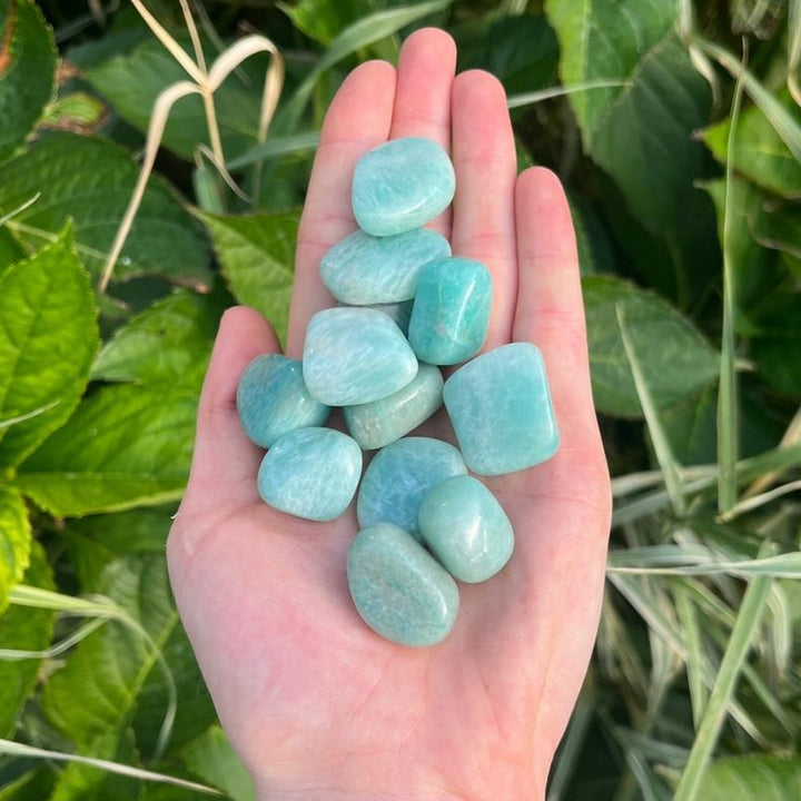 A hand holding several polished green amazonite tumbles, with a blurred green background.
