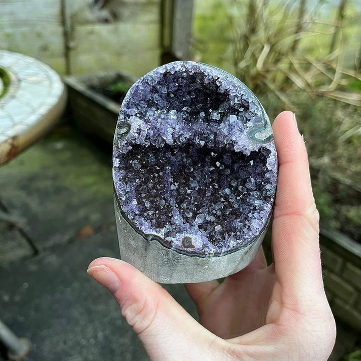 Close-up of a person holding up the freestanding amethyst crystal point, highlighting the density and deep violet coloration of the internal crystal druzy pockets.