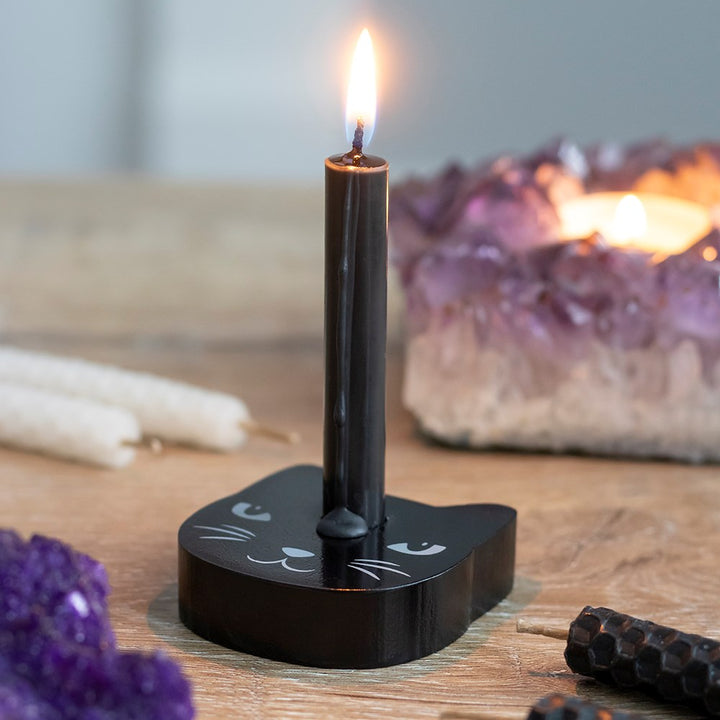 A black cat mini spell candle holder with a burning black spell candle on a wooden altar with crystals.