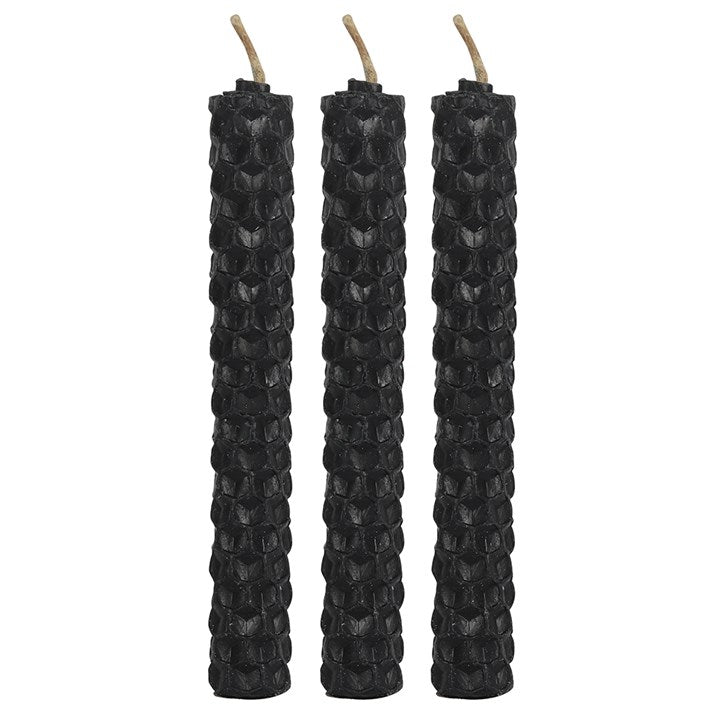 Hand holding three black textured candles with a white background