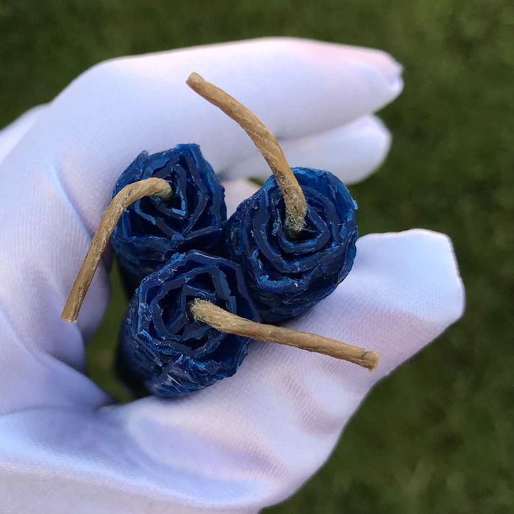 A white gloved hand holding a trio of blue beeswax ritual candles from above to show the linen wicks.