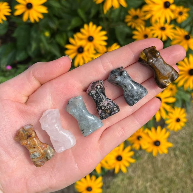 Tiger Eye Goddess Body Crystal Carvings held in a hand in a sun lit garden 