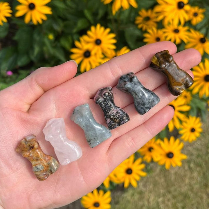 Tiger Eye Goddess Body Crystal Carvings held in a hand in a sun lit garden 