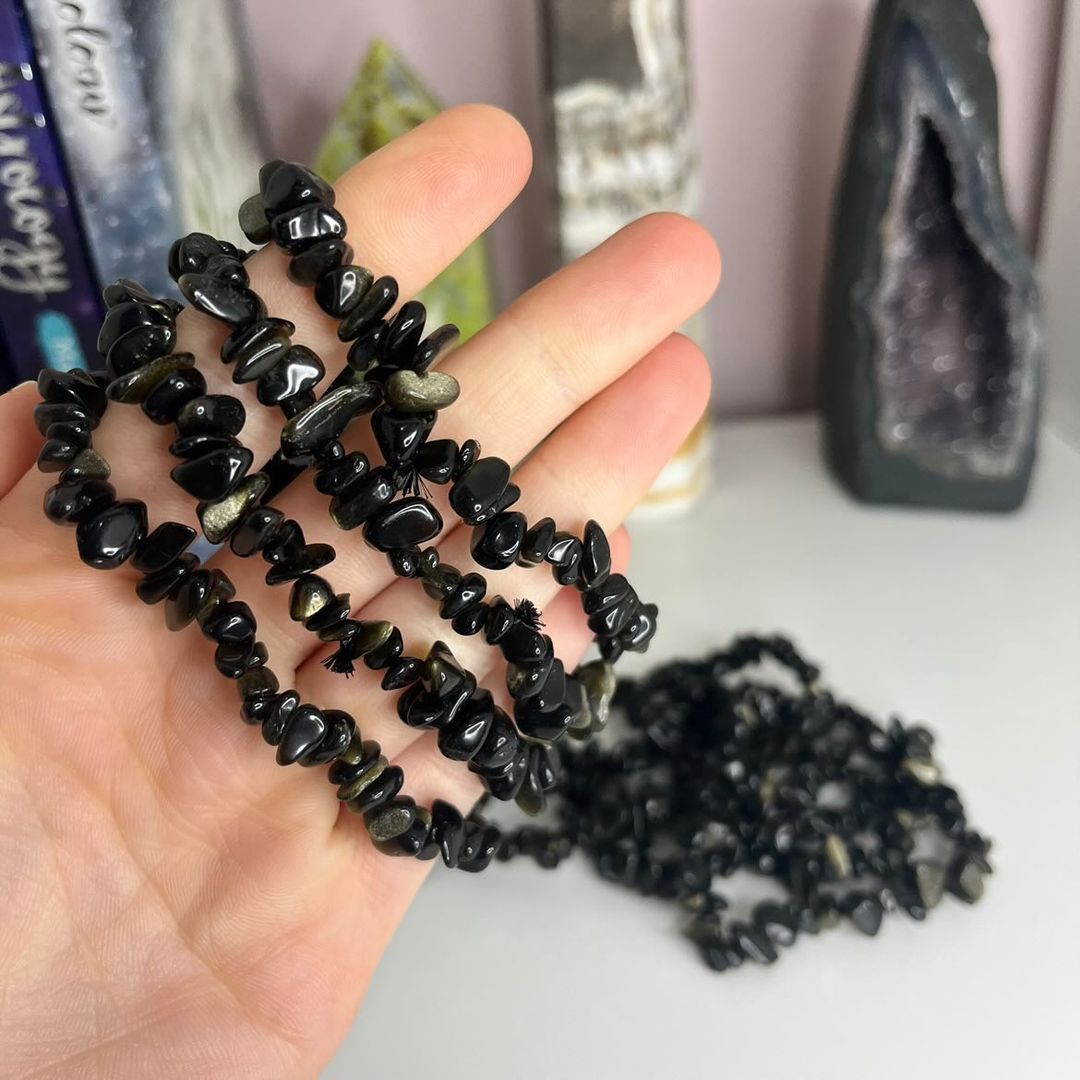 A hand holding a gold sheen obsidian crystal chip bracelet with a series of similar chips spilling out in front.
