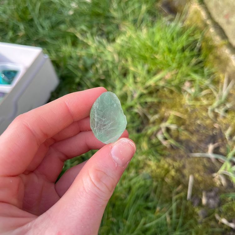 A close-up of small, rough green crystal pieces resting in a palm, highlighting their natural glass-like facets, internal frost paths, and earthy mineral textures.