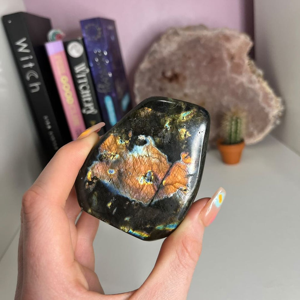 A hand holding a Labradorite Polished Freeform in front of a desk with books in the background