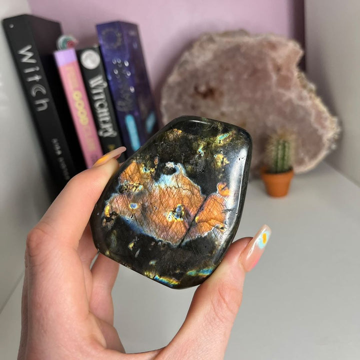 A hand holding a Labradorite Polished Freeform in front of a desk with books in the background