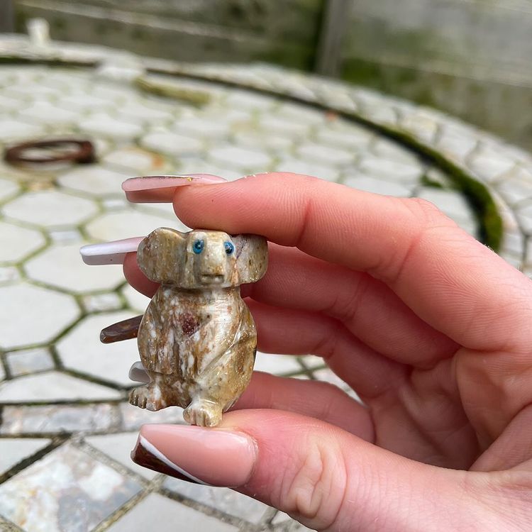 One mini soapstone koala held in a hand in a garden.