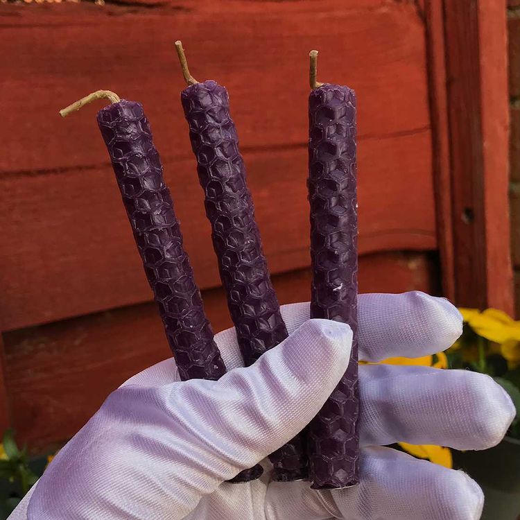 Three purple honeycomb beeswax spell candles held in a white gloved hand outdoors for prosperity rituals.