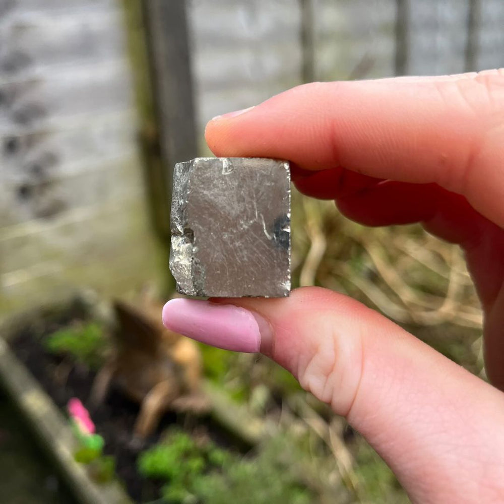 A hand holding a Raw Pyrite Cube in a sunlit garden