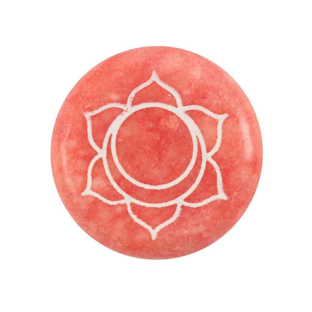 A flat, circular orange crystal meditation stone engraved with the sacred Sacral chakra symbol (Svadhisthana) highlighted in white detailing.