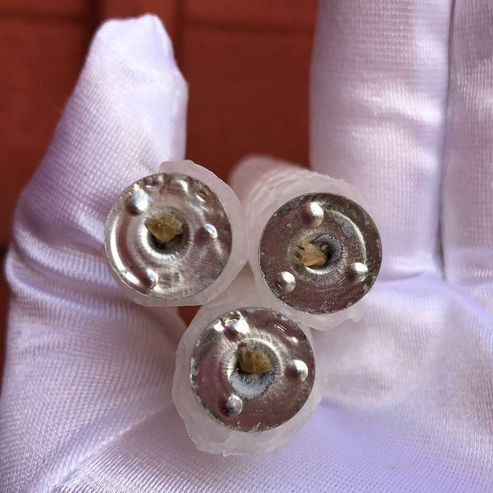 The flat circular bases and wicks of three white beeswax spell candles held closely in a white gloved hand.