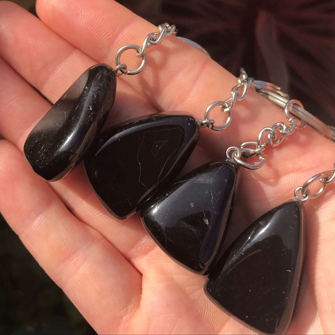 A close-up shot of four smooth, highly polished black onyx crystal keyrings lined up across an open palm outdoors.