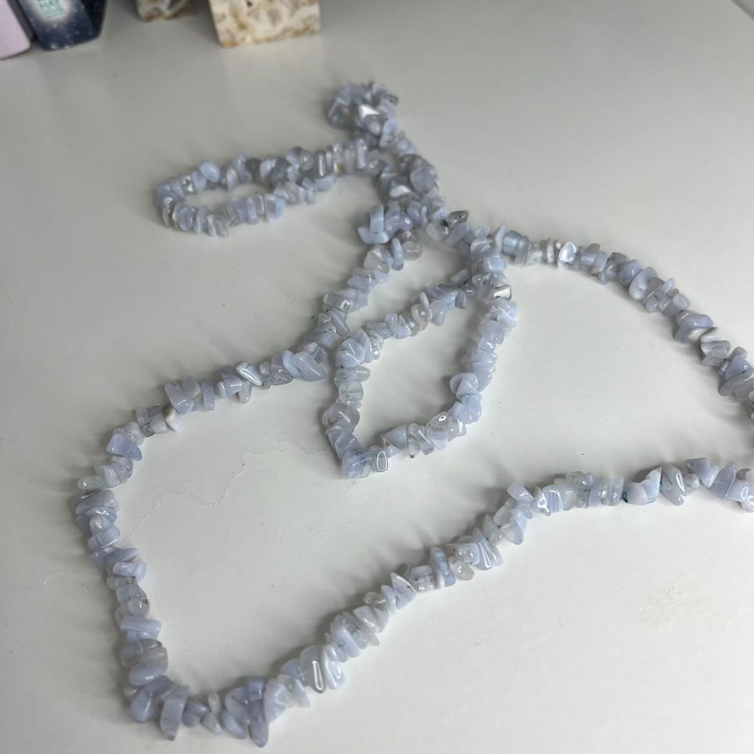 A long Blue Lace Agate crystal chip necklace laid out in loops on a smooth white surface, showcasing the continuous strand of polished, irregular gemstone chips with their soft, pale blue colour hues and subtle white mineral bands.