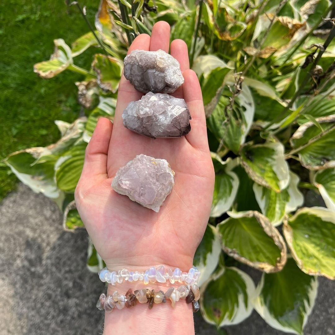 An outdoor shot of an open hand presenting three distinct prickly Spirit Quartz crystal chunks. Tracing across the rocky, bumpy surfaces under natural daylight highlights their compact companion sizing, perfect for placing on a bedroom window sill or a busy workspace desk.

