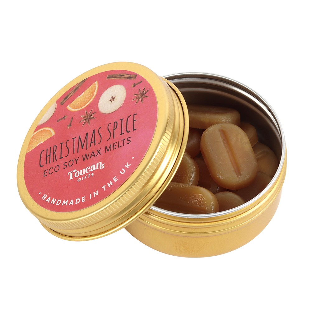 An open gold aluminium tin filled with small, pill-shaped light brown soy wax melts, with its red and gold circular product label featuring orange slice and apple illustrations leaning against the base on a white background.