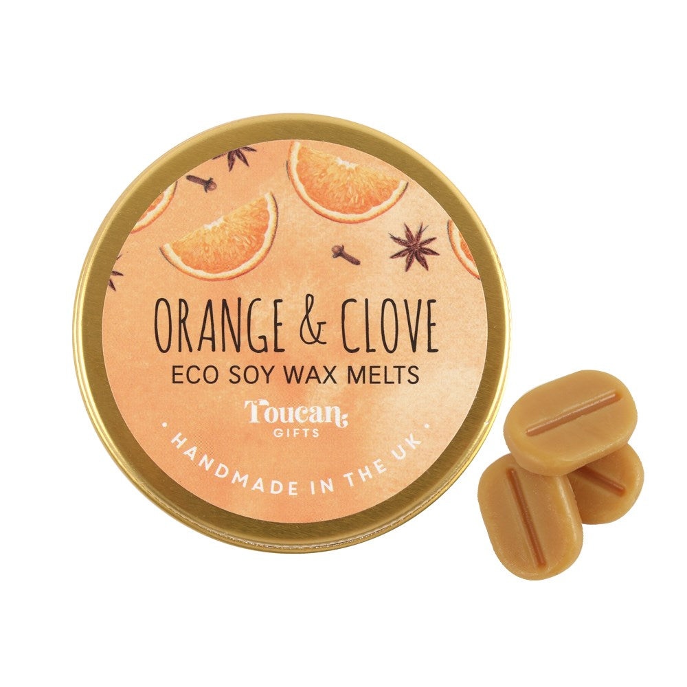 A product display shot showcasing the circular orange and gold lid of the Orange and Clove wax melts next to three loose, orange‑brown mini soy melts against a clean white background.