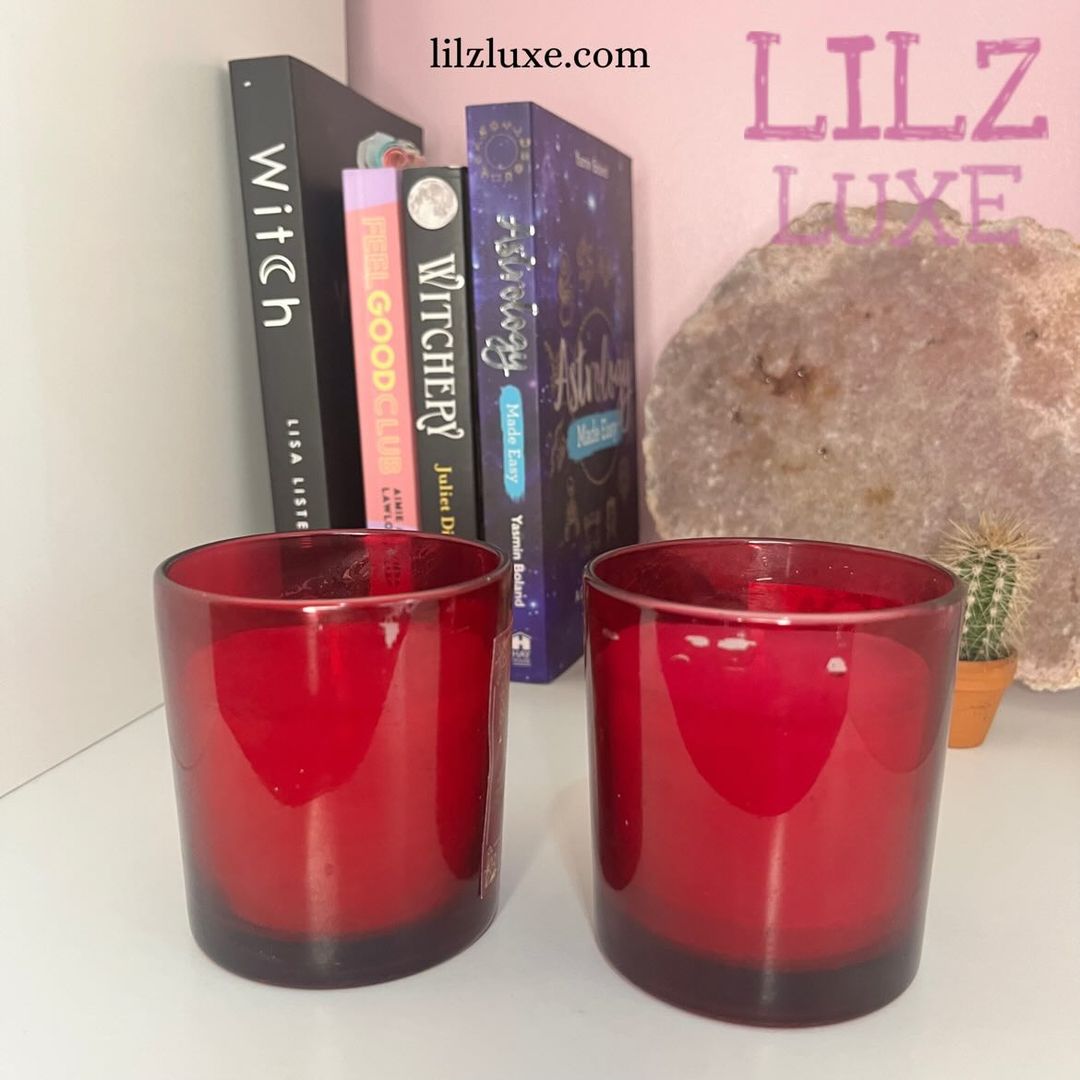 Two discounted red glass tarot card candle jars sitting side-by-side on a white surface, showcasing the translucent ruby color, metallic lids removed, and minor physical wax imperfections from the Quirky Corner collection.