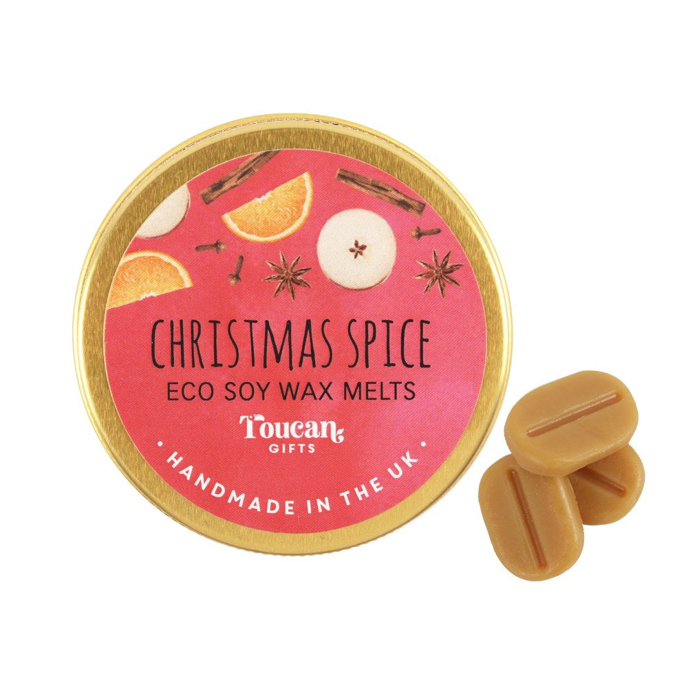 A product display shot showcasing the circular red and gold lid of the Christmas Spice wax melts next to three loose, light brown mini soy melts against a clean white background.