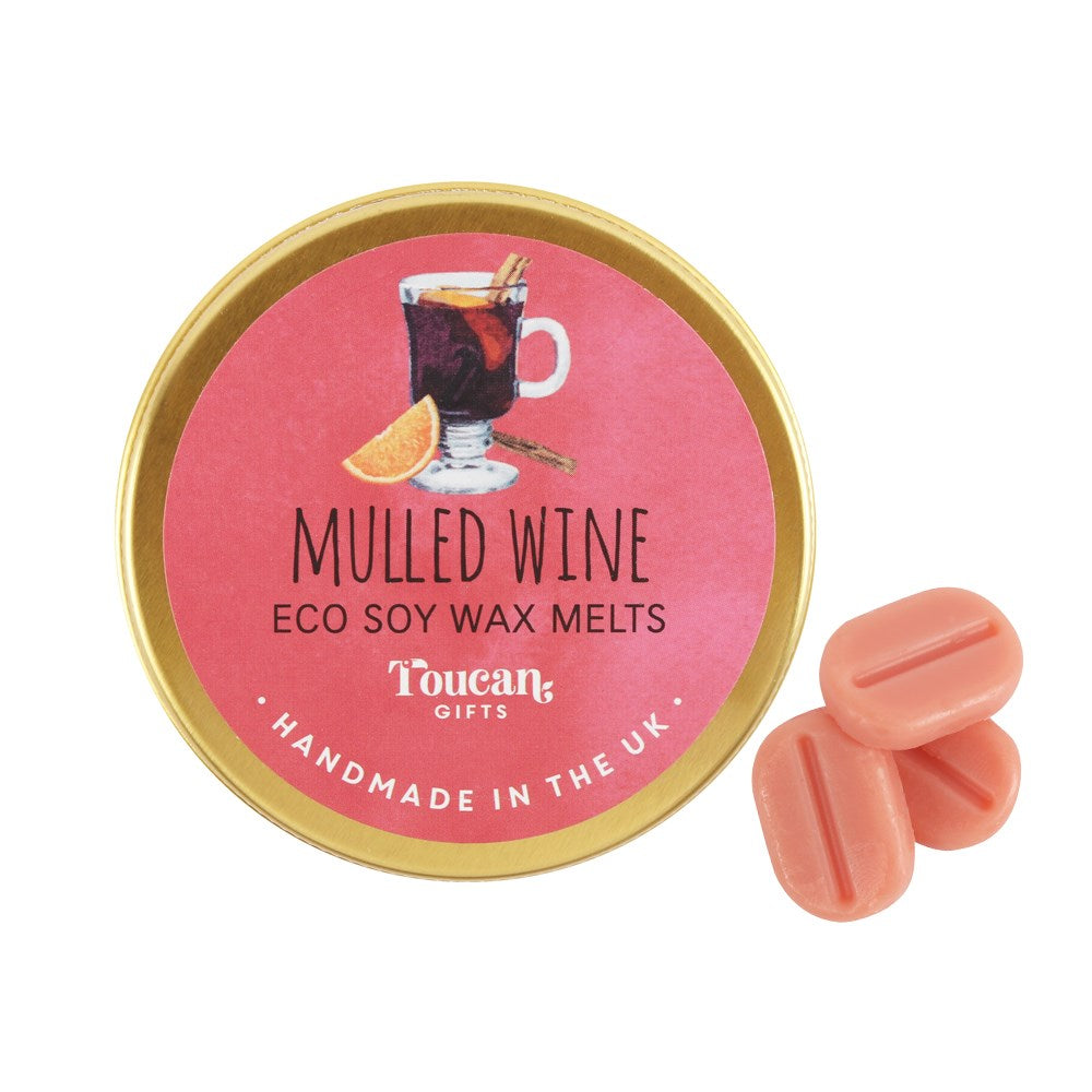 A product display shot showcasing the circular pink and gold lid of the Mulled Wine wax melts next to three loose, reddish‑pink mini soy melts against a white background.