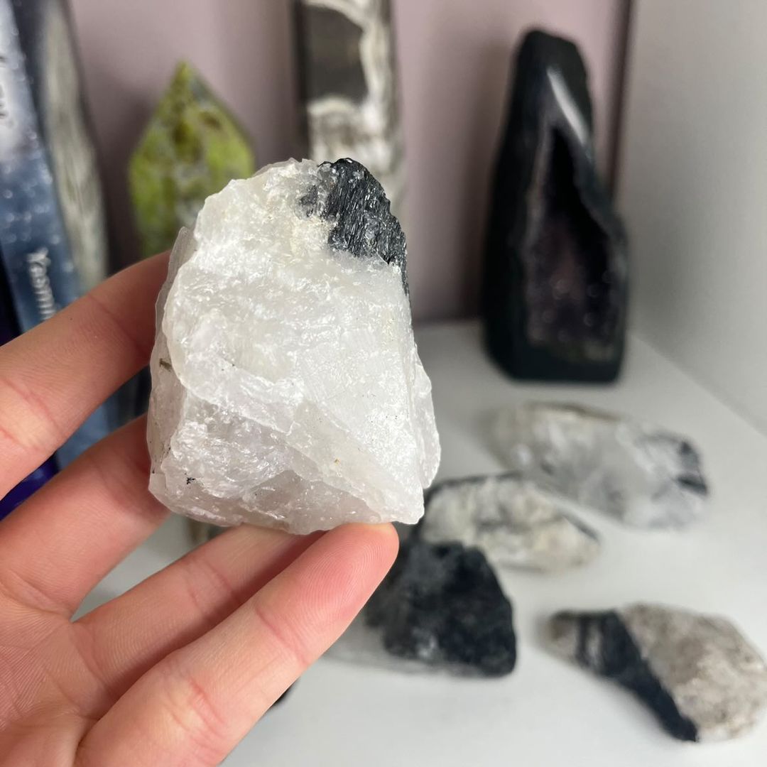 A hand holding a blocky unpolished clear quartz crystal with clean black tourmaline stripes along its edge, demonstrating the beautiful geological birthmarks of this protective, earth-born mineral powerhouse.
