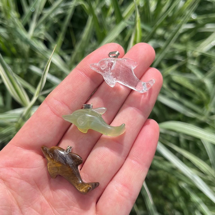 A top-down view of several miniature carved crystal animal totems resting in a palm, highlighting a light green Aventurine dolphin pendant.