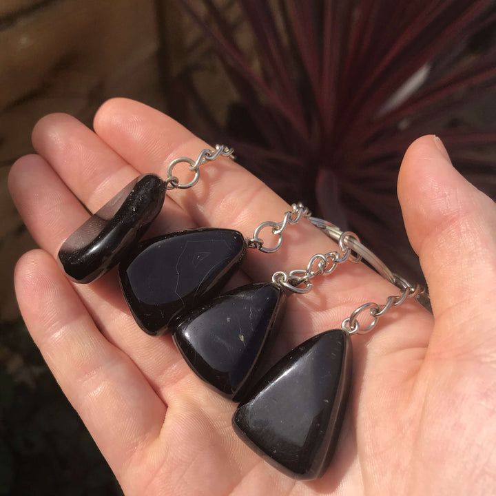 A side-angle view of four pocket-sized black onyx crystal keyrings cradled in an open palm to illustrate their sleek, glassy texture.
