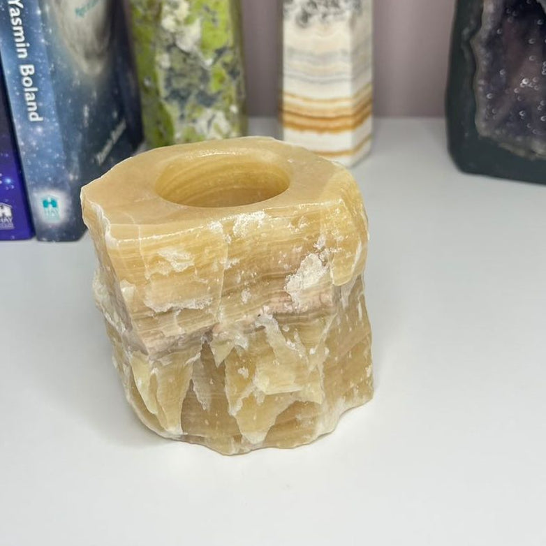 A close-up view of a natural honey-calcite tea light holder resting on a smooth surface showing its translucent texture and warm amber shades.
