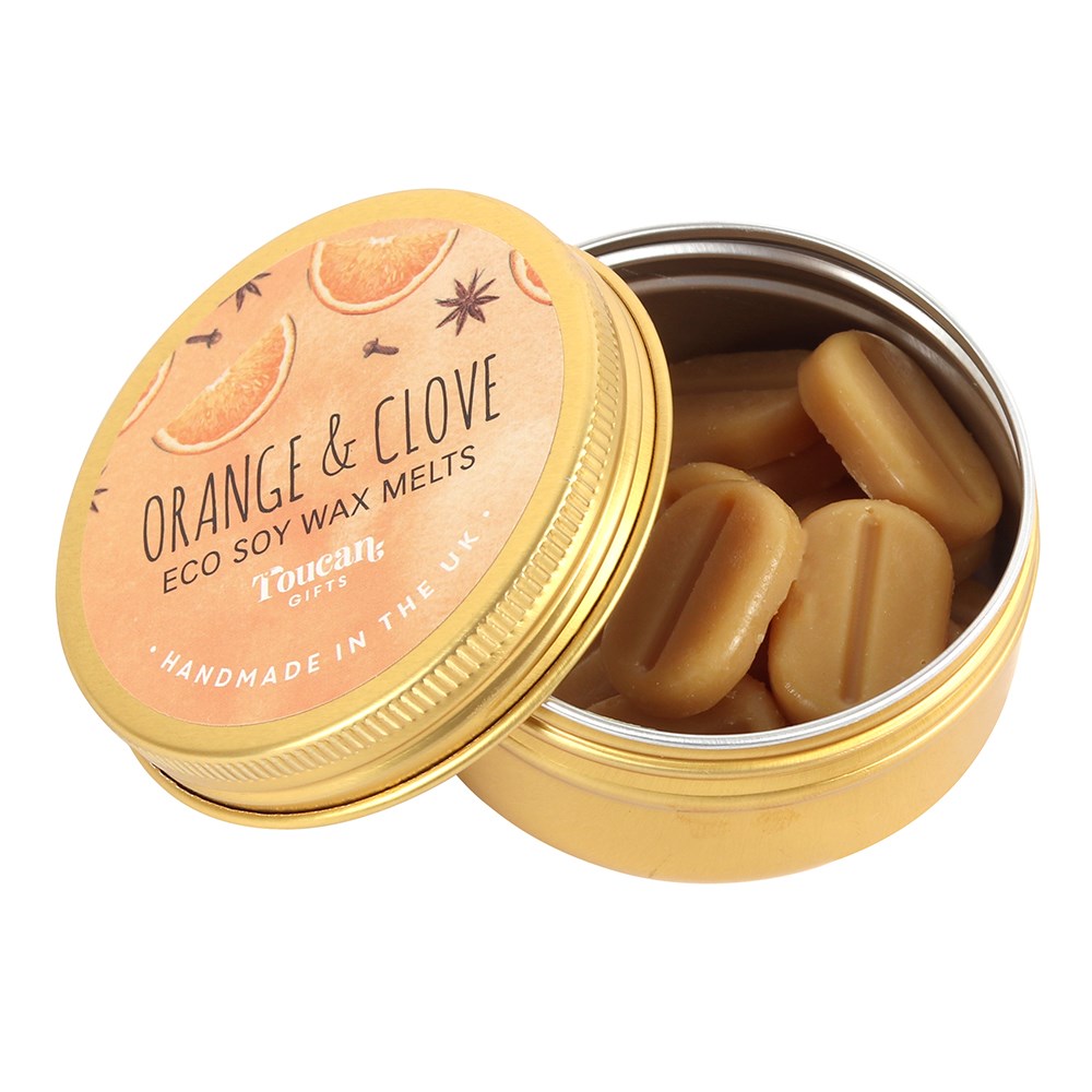 An open gold aluminium tin filled with small, pill-shaped light orange‑brown soy wax melts, with its orange‑toned circular product label featuring star anise and orange illustrations leaning against the base on a white background.