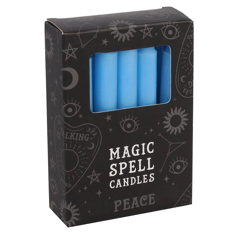 A three-quarter view of a black cardboard pack of Peace spell candles against a white background. The box displays mystical white line illustrations of eyes, suns, and moons, with a clear rectangular cutout window revealing several smooth, light blue unscented mini tapers designed to align with the Throat chakra.
